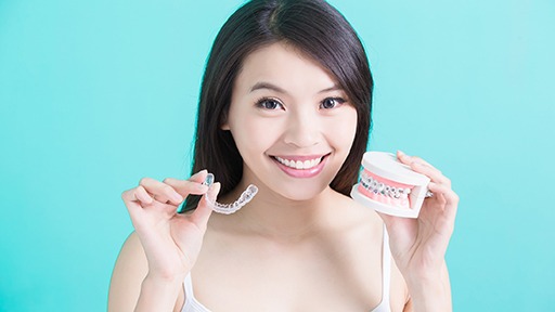 Woman holding Invisalign tray and model with of smile with braces